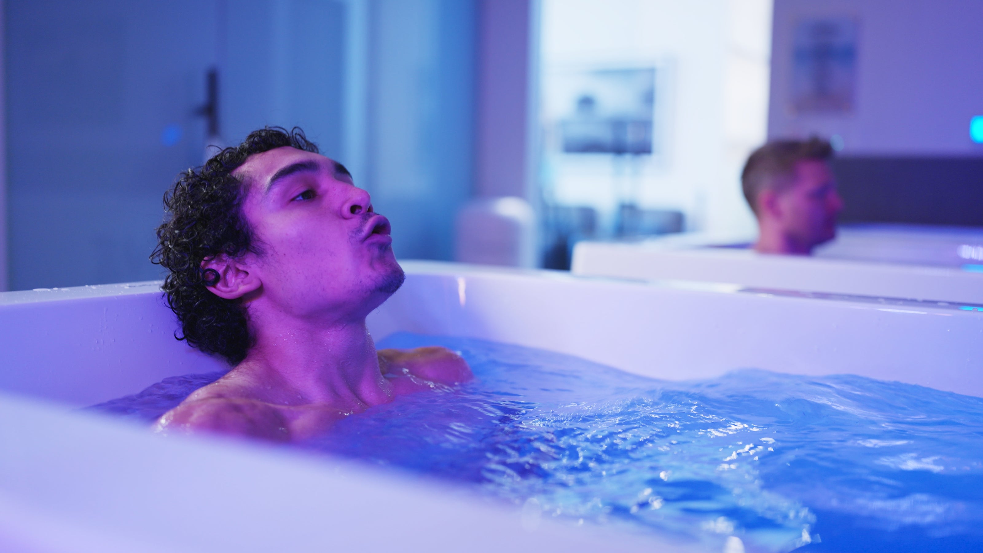 Man sitting in cold plunge, illuminated by low-purple LED lights.